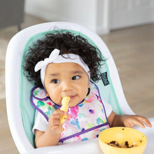 Load image into Gallery viewer, A baby with curly hair sits in a high chair wearing a colorful bib, eating from a Bumkins Silicone First Feeding Set: Pineapple.
