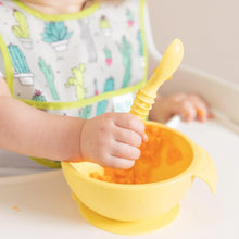 Load image into Gallery viewer, Close-up of a baby in a cactus-patterned bib eating from a Bumkins Silicone First Feeding Set: Pineapple on a high chair tray.
