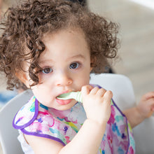 Load image into Gallery viewer, A curly-haired girl wearing a floral bib puts a Bumkins Silicone Dipping Spoons 3 Pack: Gumdrop in her mouth.

