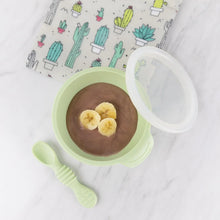 Load image into Gallery viewer, Bumkins Silicone First Feeding Set: Sage with chocolate pudding topped with bananas on a marble background next to a cactus print pouch.
