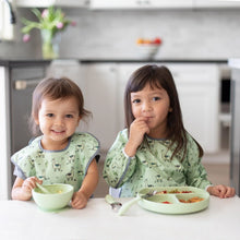 Load image into Gallery viewer, Two kids sits at a white table wearing matching green bibs with animal prints; one eats from a Bumkins Silicone First Feeding Set: Sage.
