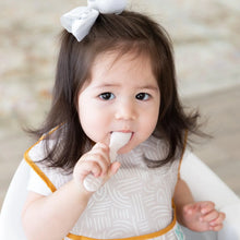 Load image into Gallery viewer, A toddler in a high chair with a white bow and bib chews a spoon from Bumkins Silicone First Feeding Set: Sand.
