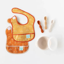 Load image into Gallery viewer, Bumkins Silicone First Feeding Set: Sand sits among baby spoons and colorful bibs on a white background.
