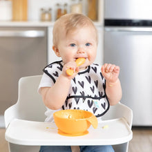 Load image into Gallery viewer, A baby in a high chair wearing a heart-patterned bib eats from a Bumkins Silicone First Feeding Set: Tangerine.

