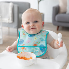 Load image into Gallery viewer, A baby wearing a Bumkins Starter Bib 2 Pack: Ocean Life &amp; Whale Tail sits in a high chair, eating mashed sweet potatoes from a white bowl.
