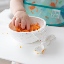Load image into Gallery viewer, A baby's hand reaches into a Bumkins Silicone First Feeding Set: Vanilla Sprinkle filled with mashed sweet potato with a spoon beside it.
