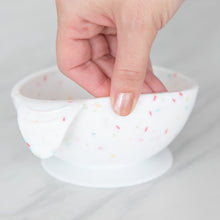 Load image into Gallery viewer, A hand holds a Bumkins Silicone First Feeding Set: Vanilla Sprinkle, demonstrating the suction cup bottom on a marble surface.
