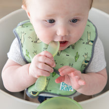 Load image into Gallery viewer, A baby in a high chair wearing a green bib chews the spoon of a Bumkins Silicone First Feeding Set: Green Jelly.

