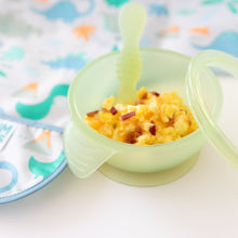 Load image into Gallery viewer, Close-up of Bumkins Silicone First Feeding Set: Green Jelly filled with scrambled eggs &amp; bacon next to a dinosaur bib on a white background.
