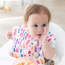Load image into Gallery viewer, In a high chair, a baby with a colorful bib enjoys messy mealtime using Bumkins Silicone First Feeding Set: Pink Jelly.
