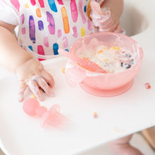 Load image into Gallery viewer, Close-up of a child in a high chair reaching for a Bumkins Silicone Chewtensils®: Pink Jelly while messily eating yogurt and fruit from a bowl.
