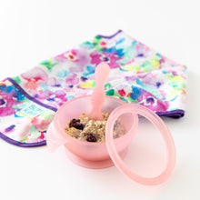 Load image into Gallery viewer, Bumkins Silicone First Feeding Set: Pink Jelly, filled with oatmeal and berries, sits next to a folded floral bib on a white background.
