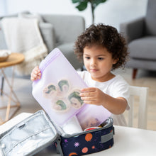 Load image into Gallery viewer, A curly-haired child packs food into a space-themed lunchbox with Bumkins Silicone Flat Reusable Bag 2 Pack, Lavender in a bright room.
