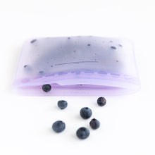 Load image into Gallery viewer, Blueberries spill out of an open Bumkins Silicone Flat Reusable Bag 2 Pack, Lavender on a white background.
