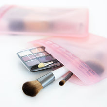 Load image into Gallery viewer, Makeup brushes and an eyeshadow palette peek out from Bumkins Silicone Flat Reusable Bag 2 Pack, Pink on a white background.
