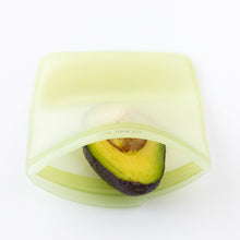 Load image into Gallery viewer, A half avocado sits in an open Bumkins Silicone Flat Reusable Bag 2 Pack, Sage on a white background.
