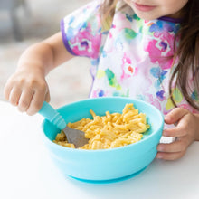 Load image into Gallery viewer, A toddler eats mac and cheese from Bumkins Silicone Grip Bowl: Blue at a white table, while wearing a vibrant bib.

