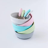 Five bowls and spoons, including Bumkins Silicone Grip Bowl: Gray, sit stacked on a white background.