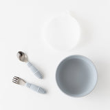 Bumkins Silicone Stretch Lid for Grip Bowl  lays above a gray bowl and gray toddler utensils on a white background.