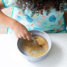 Load image into Gallery viewer, A child enjoys applesauce from Bumkins Silicone Grip Bowl: Gray, spoon in hand, wearing a colorful ocean-themed bib at a white table.
