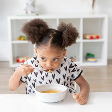 Load image into Gallery viewer, A girl in pigtails wearing a black &amp; white patterned bib eats soup from a Bumkins Silicone Grip Bowl: Marble with a spoon at a white table.
