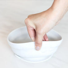 Load image into Gallery viewer, A hand holds a Bumkins Silicone Grip Bowl: Marble, demonstrating the suction cup bottom on a marble surface.
