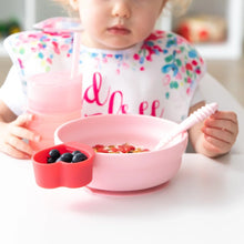 Load image into Gallery viewer, A toddler enjoys breakfast with from Bumkins Silicone Grip Bowl: Pink, with a matching cup and utensils, at a white table.
