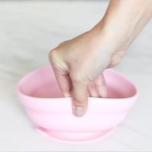 Load image into Gallery viewer, A hand holds a Bumkins Silicone Grip Bowl: Pink, demonstrating the suction cup bottom on a marble surface.
