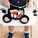 Close-up of a child in a high chair with cereal, fruit, and oatmeal in a Bumkins Silicone Grip Dish: Mickey Mouse; utensils sit close by.