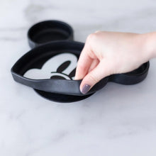 Load image into Gallery viewer, A hand holds a Bumkins Silicone Grip Dish: Mickey Mouse, demonstrating the suction cup bottom on a marble surface.
