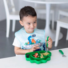 Load image into Gallery viewer, A child enjoys fruit and pasta from a Bumkins Silicone Grip Dish, Special Edition: Dino with a fork, wearing a blue bib at a white table.
