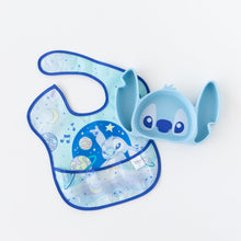 Load image into Gallery viewer, Bumkins Silicone Grip Dish: Stitch lays beside a blue Stitch space-themed bib on a white background.
