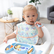 Load image into Gallery viewer, A boy in a pastel bib uses a fork to eat eggs and orange slices from a Bumkins Silicone Grip Dish: Stitch in a cozy living room.
