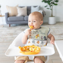 Load image into Gallery viewer, A baby in a high chair happily tackles meal time with a yellow spoon and Bumkins Silicone Grip Dish: Winnie The Pooh in a cozy living room.
