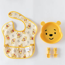 Load image into Gallery viewer, Bumkins Silicone Grip Dish: Winnie The Pooh sits near matching utensils and a yellow bear-print bib on a white background.

