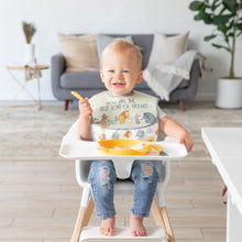 Load image into Gallery viewer, A smiling baby in a high chair, wearing a bib, holds a spoon next to a Bumkins Silicone Grip Dish: Winnie The Pooh in a cozy living room.
