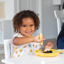 Load image into Gallery viewer, A curly-haired child joyfully eats from a Bumkins Silicone Grip Dish: Winnie The Pooh using a yellow fork at a white table.
