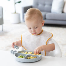 Load image into Gallery viewer, A toddler enjoys a meal from a Bumkins Silicone Grip Dish: Gray with gray toddler utensils at a white table in a bright living room.
