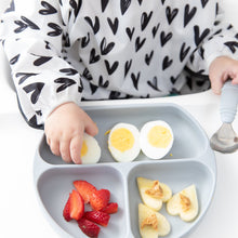 Load image into Gallery viewer, Close-up of a child in a black &amp; white heart-patterned bib eating eggs and fruit from a Bumkins Silicone Grip Dish: Gray.
