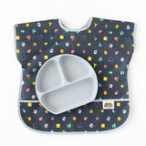 A gray divided plate sits on top of a Bumkins Junior Bib: Super Mario™ Lineup on a white background.