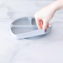 Load image into Gallery viewer, A hand holds a Bumkins Silicone Grip Dish: Gray, demonstrating the suction cup bottom on a marble surface.
