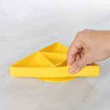 A hand holds a Bumkins Silicone Grip Dish: Zelda™ Triforce, demonstrating the suction cup bottom on a marble surface.