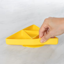 Load image into Gallery viewer, A hand holds a Bumkins Silicone Grip Dish: Zelda™ Triforce, demonstrating the suction cup bottom on a marble surface.
