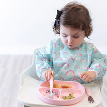 Load image into Gallery viewer, A toddler in a high chair, wearing a rainbow bib, uses pink utensils to eat fruit and pasta from a Bumkins Silicone Grip Dish: Pink.

