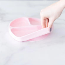 Load image into Gallery viewer, A hand holds a Bumkins Silicone Grip Dish: Pink, demonstrating the suction cup bottom on a marble surface.
