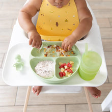 Load image into Gallery viewer, A baby in a high chair enjoys yogurt, chopped fruit, and hash browns from a Bumkins Silicone Grip Dish: Sage with utensils and a green cup.
