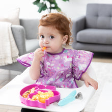 Load image into Gallery viewer, A girl wearing a purple bib in a high chair looks curiously at the camera, eating from a Bumkins Silicone Grip Dish Special Edition: Unicorn.
