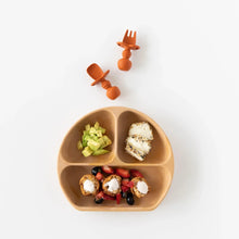 Load image into Gallery viewer, Bumkins Silicone Grip Dish: Wood Grain holds avocado, toast, and yogurt, with two orange toddler utensils above on a white background.
