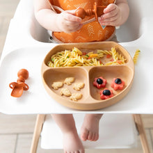 Load image into Gallery viewer, A baby in a highchair, wearing an orange bib, holds a spoon and enjoys pasta, crackers, and fruit from Bumkins Silicone Grip Dish: Wood Grain.
