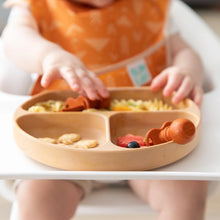 Load image into Gallery viewer, Close-up of a baby in a high chair reaching for toddler utensils in a Bumkins Silicone Grip Dish: Wood Grain filled with food.
